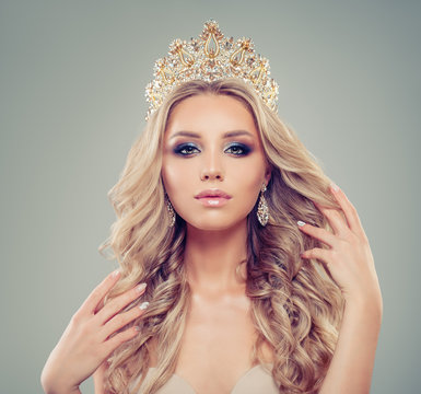 Elegant blonde woman with makeup, long healthy curly hairstyle, gold jewelry crown and earrings, portrait