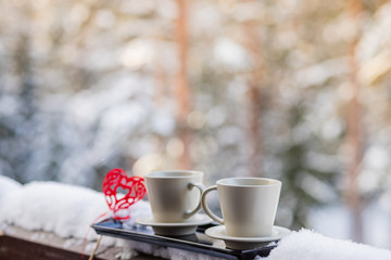 Valentine's day concept - two cups of tea,coffee,hot drink in front of snow background.two cups with hot coffee on the background of the winter forest. decorations for Valentine's Day or wedding.Copy