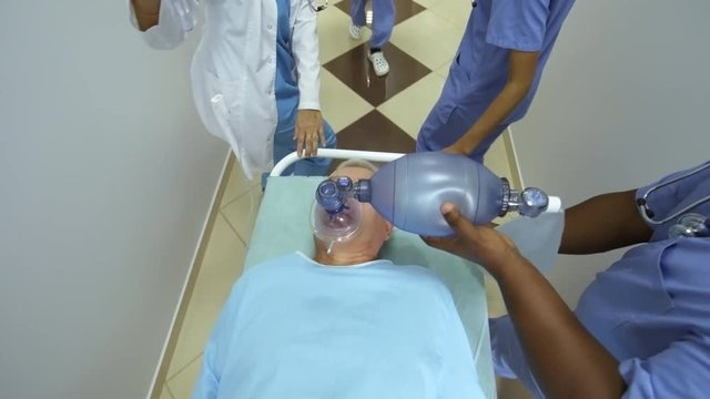 High angle dolly shot of ER nurses and female doctor pushing gurney along hospital corridor and administering oxygen and IV fluids to elderly patient