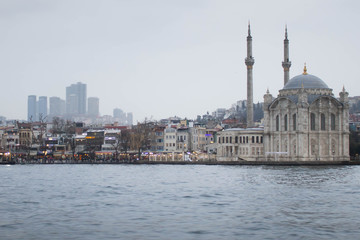 Fototapeta na wymiar Old power meets new power in form of mosque and skyscrapers. View from the river on cloudy and foggy day.