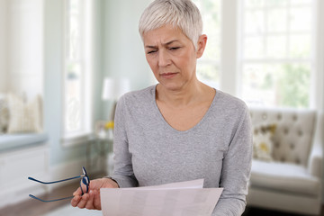 Mature woman with skeptical expression reading contract document or paying bills