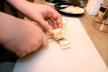 Woman hands cutting piece of cheese, she prepare food at kitchen. Chef cutting cheese with knife on wooden board on restaurant kitchen table. Housewife with a knife sliced cheese on cutting board.