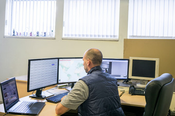 The bald guy looks at a lot of monitors. A man is sitting in the center of tracking and monitoring. Specialist in information security. System administrator of data storage servers.