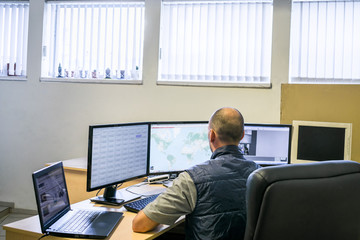 Monitoring department of a network Internet provider. A man looks at several monitors. Specialist in information security,  view from the back