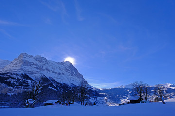 The sun hides behind the famous peak of the Eiger mountain above Grindelwald, with a lot of snow,...