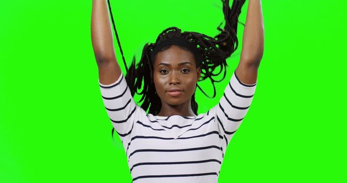 Portrait of the pretty joyful young African American girl lifting her hair with pigtails up, then letting go and smiling happily to the camera on the green screen background. Chroma key.