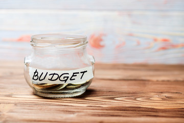 Budget. Glass jar with coins and inscription budget. Wooden background in the old style. have toning.