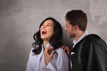 Excited laughing business woman and smiling businessman in white shirts standing with folded arms on loft style wall