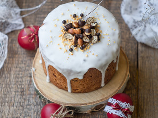 Easter cake kulich, traditional Russian Easter bread decorated white icing, chocolate and cookies, beautiful Easter food composition with red eggs on wooden background. Close up, selective focus.