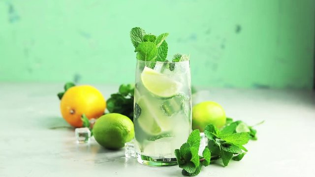 Mojito cocktail with lime and mint in highball glass on a gray and green concrete stone surface background. Close up, shallow depth of the field, 59.94 fps.