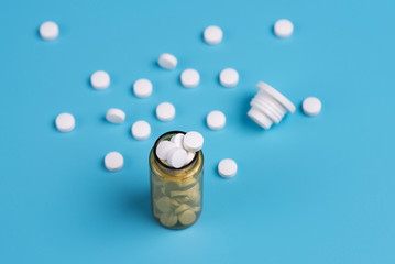 White pills in the glass bottle on a blue background.