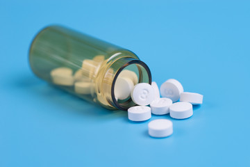 White pills in the glass bottle on a blue background.