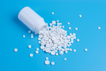 White pills, tablets and white bottle on blue background.