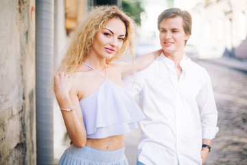 beautiful couple in love walking and gently hugging in sunny green street. stylish hipster groom and blonde bride embracing. romantic moments in summer city street on vacation