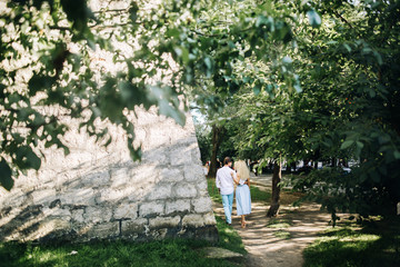 beautiful happy couple in love walking and gently hugging in sunny green street. stylish hipster groom and blonde bride embracing. romantic moments in summer city street on vacation