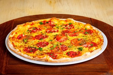 Pizza Italian pepperoni with melted cheese, salami, tomatoes and species on a white plate on a thick brown table