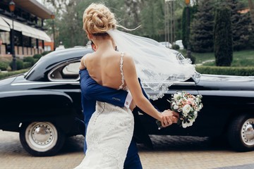 luxury wedding couple dancing at old car in light. stylish bride and groom hugging and embracing in...