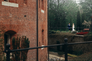 luxury wedding couple posing at old building in light. stylish bride and groom looking and embracing in city street. romantic sensual moment. woman looking at man