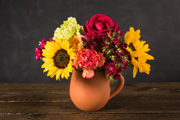 Bouquet of white yellow and red flowers in a clay pot on a dark background