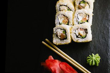Sushi rolls sprinkled with sesame seeds. Ingredients: eel, salmon, cucumber, cream cheese, nori. Japanese rolls on a black plate.