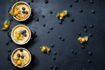 Three portions of classic English rice pudding. Blueberries and physalis. Dark background, top view, space for text