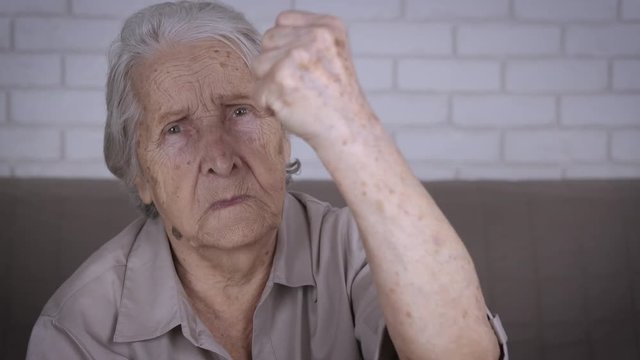 Elderly woman swears. An angry granny shows her fist.