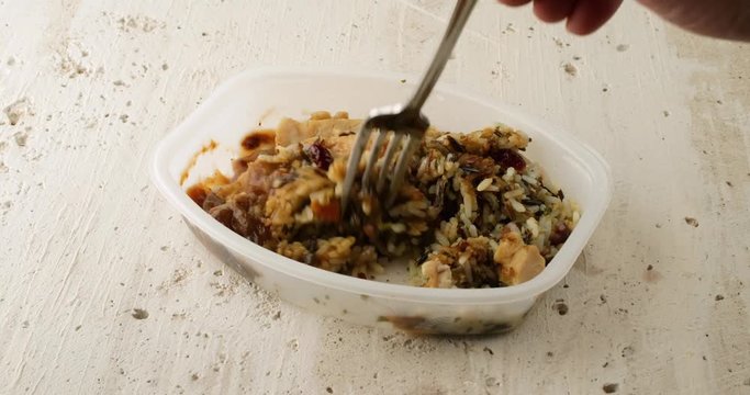 Side video of taking the film off a chicken with pecans and wild rice TV dinner in a plastic tray on a rough stone counter top illuminated with natural lighting.