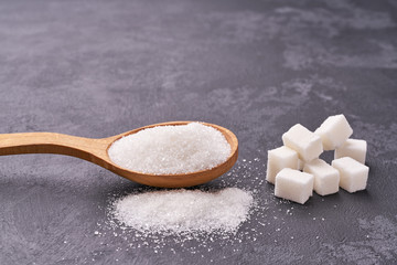 white sugar in wooden spoon on black table