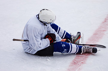 Hockey player sitting on the ice with disappointment. Tired player sitting on the ice in ice skating and hockey equipment. Professional player resting during the break. Concept of training at ice