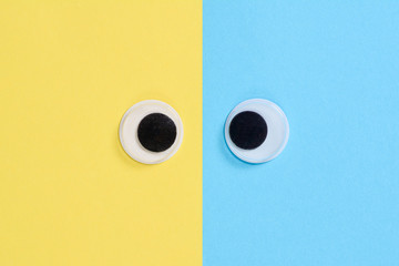 Cross-eyed googly eyes on blue-yellow background. Mad funny toys eyes close up.