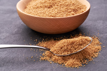 Brown sugar in a metal spoon on a black background