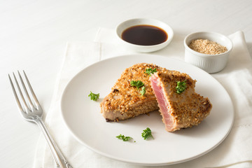 roasted tuna steak in a coat from sesame seeds, on a plate on a white table, copy space