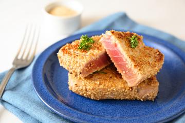 roasted tuna steak in sesame seeds with parsley garnish on a blue plate on a white table, selected focus, narrow depth of field