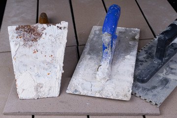 Tiles cut to size and trowels for applying mortar. Masonry accessories on a workshop table.