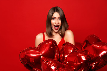 sale discount!Portrait of  positive nice cute  attractive brunette girl with wavy hair in red bikini holds a balloon in the shape of a red heart on red background,opened mouth,palms holding cheeks