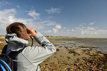Frau mit Fernglas beobachtet Vögel am Wattenmeer