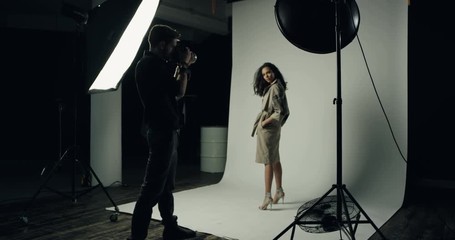Hot professional female model posing to the camera of the man photographer in the studio with spotlight.