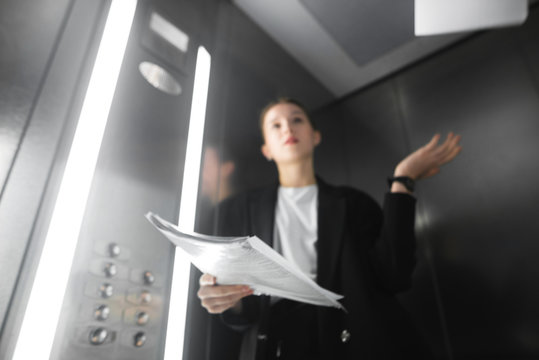 Background with a young female office worker throwing papers in the lift. Background with a businesswoman in the elevator throwing documents up. Blurry photo background.