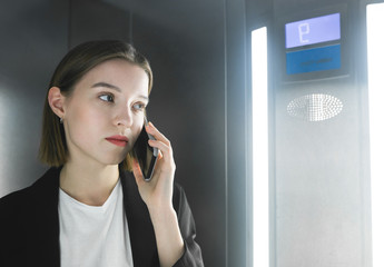 Close-up photo of ambitious office worker talking on her smartphone in the elevator. Portrait of a young female employee talking on her phone in the lift.