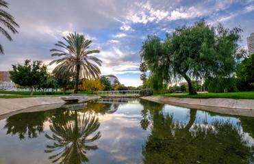 Naklejka na ściany i meble Turia river, water reflection. Valencia, Spain Gardens in the old dry riverbed of the Landscape leisure and sport area with trees, grass and water mirror