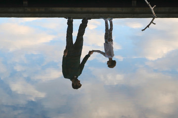 Reflection of father and daughter holding hands on a dock in the water amidst beautiful clouds