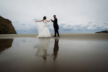 Adorable wedding couple walking along the beach, reflecting in the water. Panoramic view.