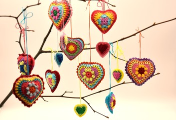 Fototapeta na wymiar Knitted hearts of colored yarn hang on a twig on a light background. Valentine's Day, love, handmade, amigurumi, hobby, decoration, postcard, creative.