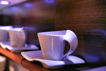 Unusual porcelain white cups and saucers displayed on a wooden shelf.