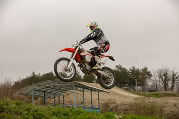 Obraz na płótnie Canvas Racer on motorcycle participates in motocross cross-country in flight, jumps and takes off on springboard against sky. Concept active extreme rest.