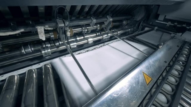 Printing machine moves paper, close up.