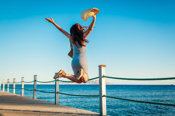 Young woman traveler jumping feeling happy and free on pier by Red sea