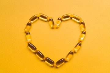Close up capsules of fish fat oil in the heart shape, omega 3, vitamin e on the yellow background....