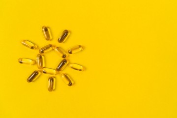 Close up capsules of fish fat oil in the sun shape, omega 3, vitamin e on the yellow background. Healthy food diet. Nutritional supplement