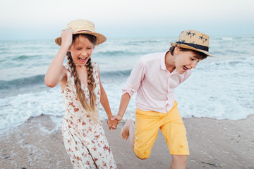 Children play and have fun on the beach. Loving teens. Romantic story on the seafront. The girl and the guy run away from the waves